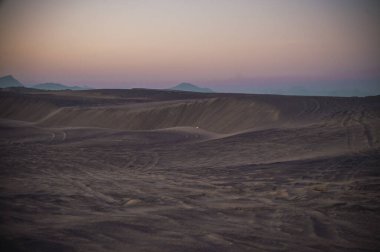 Kum tepelerinde gün batımı, güneşin son ışınlarından gelen pastel renklerle..