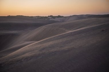 Kum tepelerinde gün batımı, güneşin son ışınlarından gelen pastel renklerle..