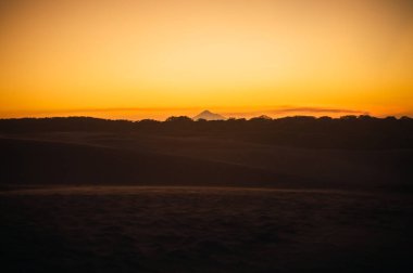 Kum tepelerinde gün batımı, güneşin son ışınlarından gelen pastel renklerle..