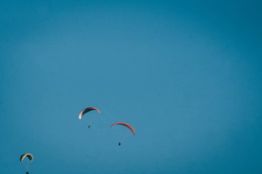 Yükseklerden süzülen paragliding bulutları ve mavi gökyüzünü görebilirsin.