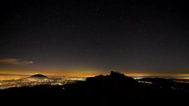 4K hızlandırılmış astrofotoğrafçılık videosu yüksek bir dağda, bir vadide bir şehir görebilirsiniz, başka bir dağ uzakta, yıldızlar kayan bir yıldızla hareket ediyor..