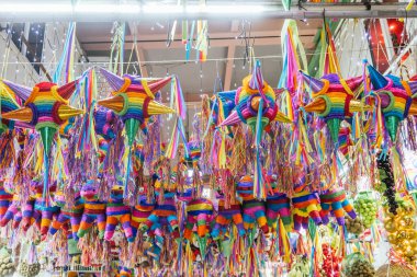 Geleneksel bir Meksika pazarının tezgahlarında farklı şekil ve boyutlarda renkli piatalar asılı..