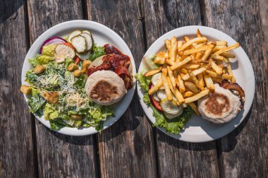 Eritilmiş peynirli hamburger, domuz pastırması ve biftek, yanında salata ve turşu, yanında da mavi peynirli burger, pastırma ve yanında patates kızartması..