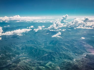 Bir uçaktan havadan fotoğraf. Dağlar, bulutlar ve bir nehrin kıyıları görülebilir..
