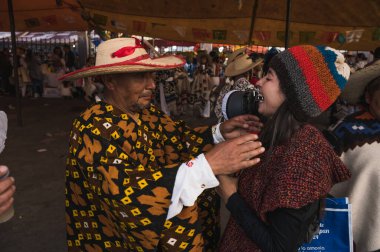 Geleneksel işlemeli bir palto giyen yerli bir adam, Guadalupe Bakiresi kutlamasına katılanlara yün şapkalar veriyor..