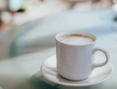 Cam bir masada beyaz bir fincanda servis edilen lezzetli kapuçino..