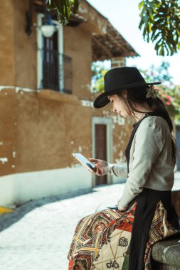 Akıllı telefonunu kontrol ederken şapkasıyla gülümseyen bir kız Meksika Eyaleti 'nin Malinalco adındaki sihirli bir kasabadaki taş ocağında oturuyor..