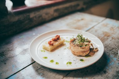 Pastırmaya sarılı fileminyon, üstüne istiridye, maydanoz, yanında da puf böreği. Beyaz bir tabakta servis ediliyor..