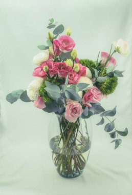 Cam bir vazonun içinde süs bitkileri olan pembe ve beyaz çiçeklerden oluşan bir buket..