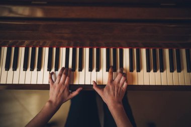 Güzel piyanist kız ahşap dik piyanosunu çalıyor, siyah ve zarif giyinmiş, mavi çiçekli küpeleri var..