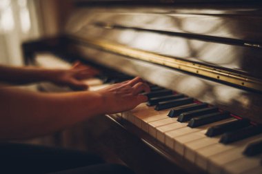 Güzel piyanist kız ahşap dik piyanosunu çalıyor, siyah ve zarif giyinmiş, mavi çiçekli küpeleri var..