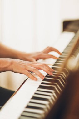 Güzel piyanist kız ahşap dik piyanosunu çalıyor, siyah ve zarif giyinmiş, mavi çiçekli küpeleri var..