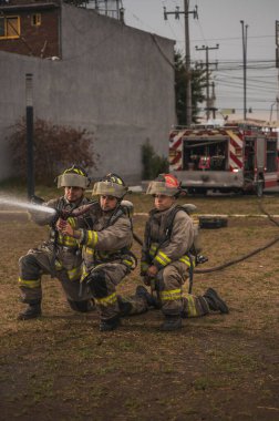 Üç cesur itfaiyeci, su perdesinin arkasında duruyor, arkalarında tanker kamyonuyla yangını söndürüyorlar..