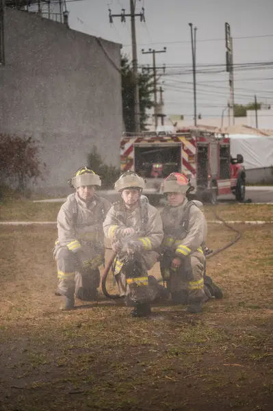 Üç cesur itfaiyeci, su perdesinin arkasında duruyor, arkalarında tanker kamyonuyla yangını söndürüyorlar..