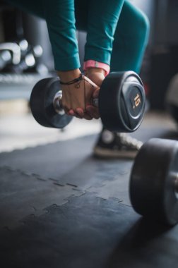 Yeşil spor giyinmiş Latin bir kız. Kalça ve bacak egzersizleri yapıyor. Çömelme ve dambıllarla..