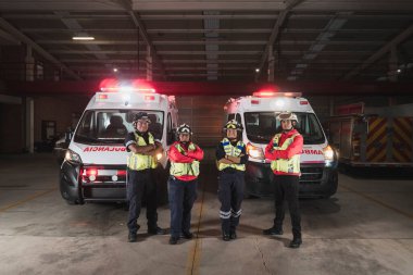 Dört Latin erkek ve kadın sağlık görevlisinden oluşan bir grup, destansı bir poz vererek hayat kurtarmaya hazır bir çift ambulansın önünde duruyor..