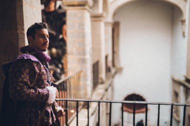 Eski bir malikanenin ikinci katındaki antika korkulukta 1600 'lü yıllardan kalma giysileri olan yakışıklı bir adam..