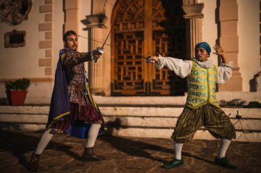 Geleneksel koloni elbiseli İspanyol erkekleri 1600 'lerin geleneksel kasabasında kılıçlarla düello yapıyorlar..