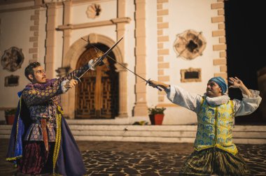 Geleneksel koloni elbiseli İspanyol erkekleri 1600 'lerin geleneksel kasabasında kılıçlarla düello yapıyorlar..