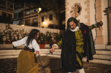 İspanyol erkek ve kadın geleneksel koloni kıyafetleri içinde kılıçlarla düello yapıyorlar. Folyo ve hançer denilen geleneksel 1600 'lü yılların şehir ortamında..