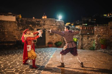 Geleneksel koloni elbiseli İspanyol erkekleri 1600 'lerin geleneksel kasabasında kılıçlarla düello yapıyorlar..