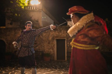 Geleneksel koloni elbiseli İspanyol erkekleri 1600 'lerin geleneksel kasabasında kılıçlarla düello yapıyorlar..