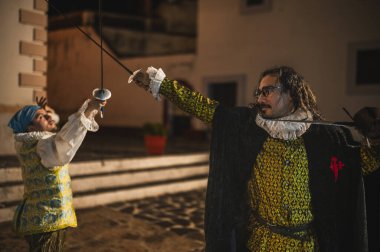 Geleneksel koloni elbiseli İspanyol erkekleri 1600 'lerin geleneksel kasabasında kılıçlarla düello yapıyorlar..