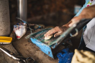 Beyaz işlemeli bluz ve mavi süveter giyen Meksikalı bir kadın geleneksel Meksika yemeği olan tortilla yapmak için tortilla makinesine hamur sıkıştırıyor..