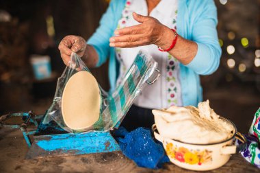 Beyaz işlemeli bluz ve mavi kazak giyen Meksikalı bir kadın geleneksel bir Meksika yemeği olan tortilla yapmak için plastik presten hamuru çıkarıyor..