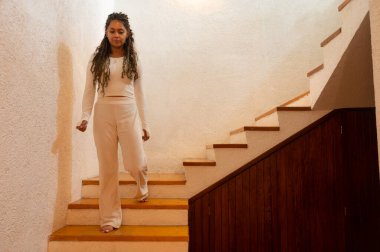 Saçları örgülü, beyaz giyinmiş, merdivenlerden inen güzel esmer Latin kız..