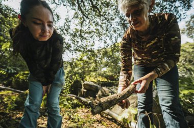 Anne ve kızı yürüyüş kıyafetleri içinde yağmur ormanlarının ortasındaki dev bir kayanın üzerinde duran dev bir ağacın yanında yürüyorlardı..