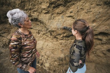 Anne ve kızı yürüyüş kıyafetleri giyip mağara resimleri bulmak için uçurumda yürüyorlar..