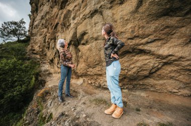Anne ve kızı yürüyüş kıyafetleri giyip mağara resimleri bulmak için uçurumda yürüyorlar..