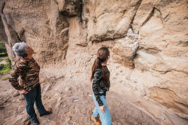 Anne ve kızı yürüyüş kıyafetleri giyip, bir uçurum boyunca yürüyüp mağara resimlerini izliyorlar..