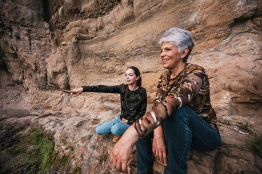 Anne ve kızı ormanda bir öğleden sonranın tadını çıkarıyor, bir uçurumda oturuyor ve ufka bakıyor..