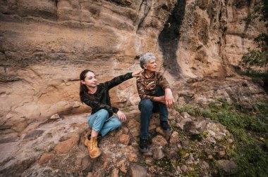 Anne ve kızı ormanda bir öğleden sonranın tadını çıkarıyor, bir uçurumda oturuyor ve ufka bakıyor..