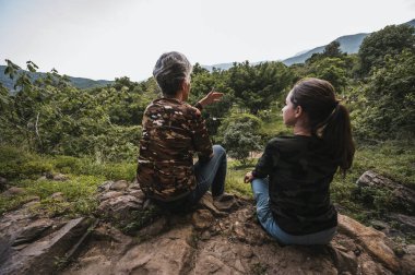 Anne ve kızı ormanda bir öğleden sonranın tadını çıkarıyor, bir uçurumda oturuyor ve ufka bakıyor..