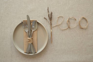 Ev dekorasyonu, doğal yaşam tarzı, ziyafet dekorasyonu, çevre dostu, sonbahar konsepti. Seramik tabak, kağıt peçetedeki metal çatal bıçak seti, kuru lavanta, eko kelimesi masa örtüsündeki iple yazılır..