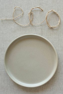 Mutfak dekorasyonu, tarz, sıfır israf yaşam tarzı, yemek blogu konsepti. Doğal kumaştan yapılmış bej masa örtüsünün üzerindeki boş seramik tabak. Eko - kelime sicimle yayıldı. Üst Manzara. Uzayı kopyala Modelleme. Kimse..