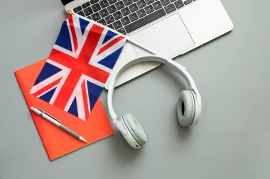 Concept of online learning English, foreign languages, distance education, knowledge, modern technologies for study. Laptop, English flag, headphones, notebook. Grey background. Copy space. Nobody. clipart