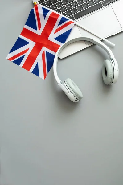 The concept of online learning English, foreign languages, distance education, knowledge, modern technologies for study. Laptop, English flag, headphones. Grey background. Vertical. Nobody.