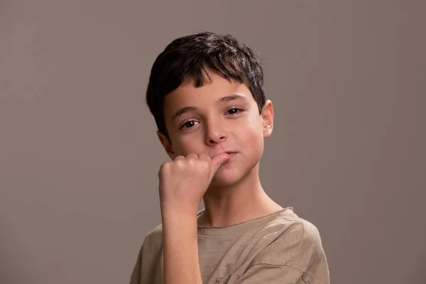 Portrait of a boy biting his nails. Studio beige background. Caucasian child, school age. Concept of nervousness, anxiety, bad habits, stress, childhood, hand hygiene.