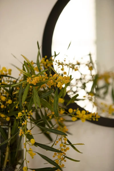 Bouquet of wild yellow flowers, acacia branches in a vase, reflected in the mirror. Stylish cozy home concept. Nobody. Daylight. Selective focus. Indoor.