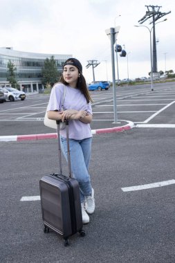 Otoparkta duran bavullu kız. Öğrenci çalışmak için geldi. Üniversite kampüsü. Dışarı çıkın. Beyaz bir kadın. Doğal güzellik. Şehir alanı. Seyahat, eğitim, tatil kavramı.