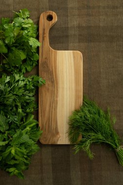 Bir sürü taze ot, kahverengi masa örtüsü üzerinde ahşap bir tahta. Üst Manzara. Nane, maydanoz, dereotu, kişniş. Yemek arkaplanı. Beslenme, yeşillik, yemek pişirme, organik konsept. Model yap. Uzayı kopyala Kimse.