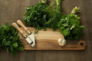 Taze maydanoz, nane ve kişniş, sarımsak karanfili ve boş çim kesme tahtasının etrafında sarımsak ezici. Yemek arkaplanı. Yemek blogu konsepti, menü, mutfak, yemek pişirme. Hiç kimse. Üst görünüm. 