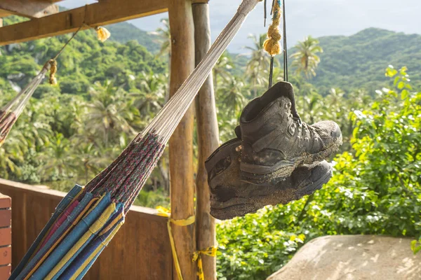 Muddy and dirty Hiking Boots hanging in the air by their shoe laces next to a hammock at Tayrona national park in Columbia, South America. Green rainforest jungle in the background