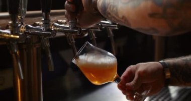 Barmen bira musluğundan bardağa bira döküyor. Ağır çekim. Bira bardağa döküldü..