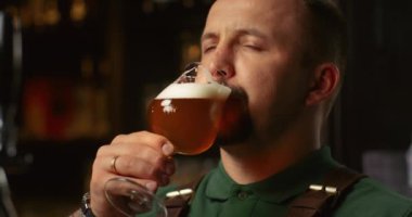 Başarılı sakallı işadamı bira tankından yeni demlenmiş biranın kalitesini kontrol ediyor.
