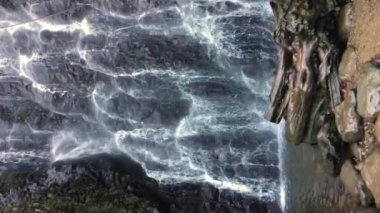 Vertical video: Slow motion of little waterfall inside canyon, water jets falling with stone wall background, between mossed rocks. Waterfall Mirveti in the Georgia mountains